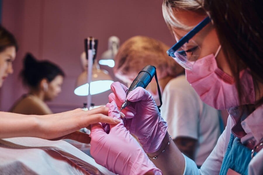 Manicurist using a nail buffer on a client. Learn more about the manicure courses near you.