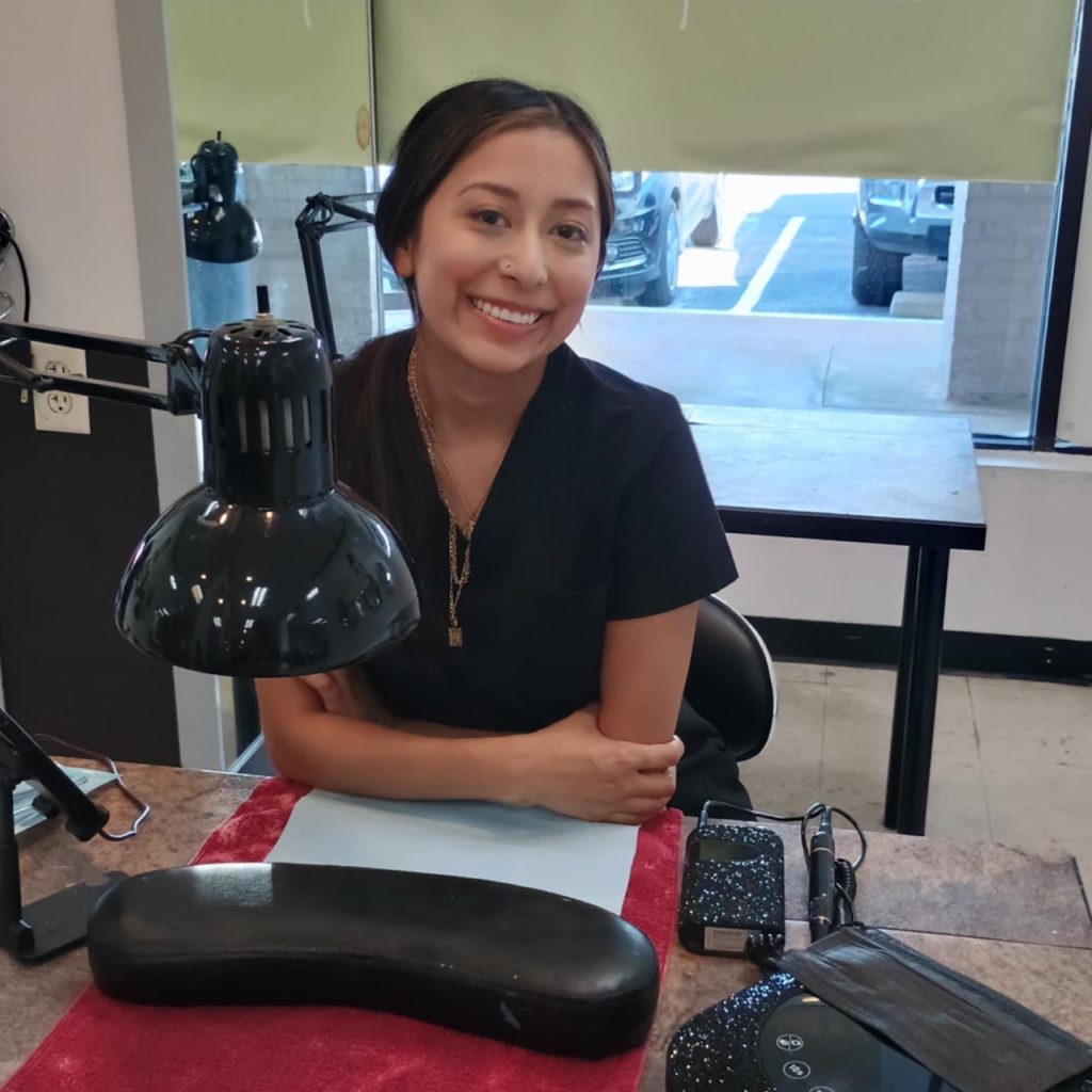att.vXMT1X178VWESwxjG6H6aD-ANhyh3ts-kj8f6JcFAos A Nuvani nail student smiling at her station